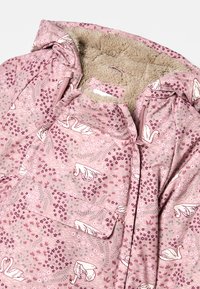 Rosa jakke med en svane- og blomstermønster, med en myk, strukturert fleecefôr og en glidelås foran. Designet inkluderer en flat lomme.