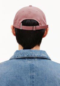 Rosa Baumwollkappe mit verstellbarem Riemen auf der Rückseite, von hinten betrachtet. Kombiniert mit einer blauen Jeansjacke. Einfaches Design.