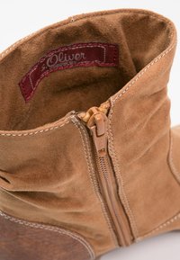 Beige Wildlederschuh mit seitlichem Reißverschluss, verstärkter Naht und weicher Innensohle. Besitzt eine abgerundete Zehenpartie und eine leicht strukturierte Oberfläche.