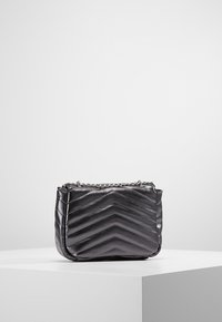 Borsa a tracolla nera trapuntata con design a chevron, realizzata in materiale liscio, dotata di una tracolla in catena argentata e di forma rettangolare.