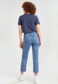 Merinvärd t-shirt i cropped stil som matchas med högmidjade ljusblå denimjeans. Jeansen har raka ben och två bakfickor. Vita sneakers.