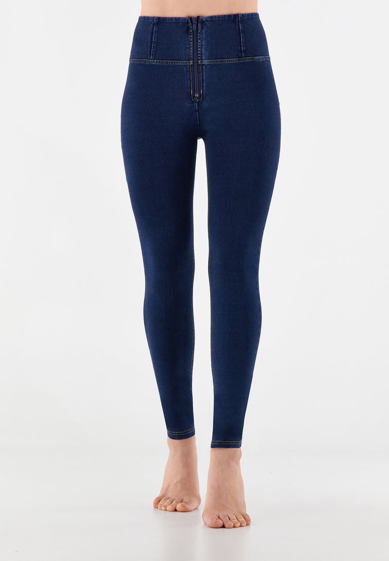 Leggings a vita alta blu navy realizzati in tessuto denim con una texture liscia, dotati di chiusura con zip frontale e cuciture gialle in contrasto.