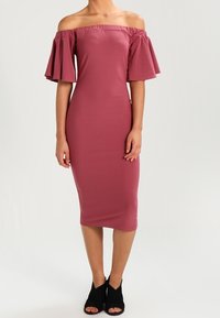 Robe ajustée, épaules dénudées, couleur vieux rose, avec manches courtes évasées. Tissu doux et extensible, longueur au genou. Escarpins noirs à bout ouvert.