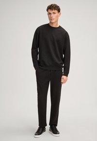 Set di felpa e pantaloni neri, caratterizzato da un sottile motivo in rilievo, scollatura ampia, polsini a coste e abbinato a sneakers nere.