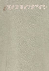 Top verde claro con tejido texturizado que presenta la palabra "amore" en cursiva brillante de color beige metálico en la parte delantera.