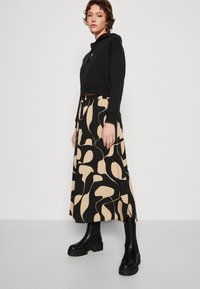 Moletom cropped preto combinado com uma saia longa de padrão em bege e preto, apresentando formas abstratas e fendas laterais, usado com botas plataforma pretas.