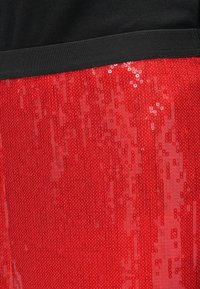 Ceinture en tissu noir au-dessus d'une jupe à sequins rouge vif, montrant un contraste de texture clair entre les matières mates et brillantes.