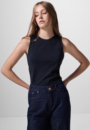 Schwarzes ärmelloses Top aus Baumwolle, kombiniert mit hochgeschnittenen dunkelblauen Jeans aus Denim mit Fronttaschen und Kupferknopf-Akzenten.