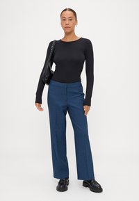 Zwarte lange mouwen bodysuit, gecombineerd met wijde blauwe broek. De outfit heeft een strak ontwerp, een gladde textuur en een zwarte schoudertas.