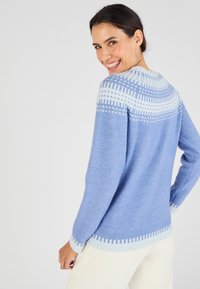 Pull bleu avec une texture douce, orné d'un empiècement blanc à motifs et de poignets contrastants. Le design inclut des rayures horizontales et verticales.