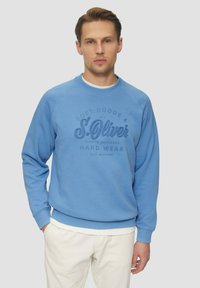 Felpa azzurra chiara realizzata in materiale morbido, con collo rotondo, polsini a costine e una stampa del logo testurizzata in blu scuro.