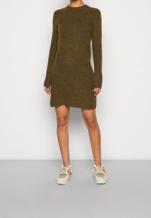 Abito a maglia color verde oliva, con maniche lunghe, scollo rotondo e una forma leggermente svasata. Abbinato a sneakers beige.