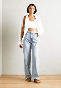 Wit cropped shirt over een witte top, gecombineerd met lichtblauwe hoge taille flare jeans en bruine sandaal. Eenvoudig, ontspannen ontwerp.