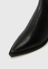 Fekete bőr, hegyes orrú bokacsizma, letisztult dizájnnal, sima felülettel és alacsony, téglalap alakú sarokkal.