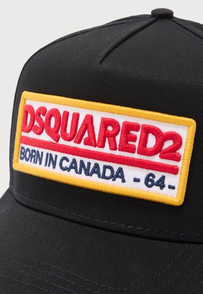 Μαύρο καπέλο με κεντημένη ορθογώνια επιγραφή που αναγράφει "DSQUARED2" με κόκκινα γράμματα και "BORN IN CANADA - 64 -" με μπλε γράμματα, με κίτρινο περίγραμμα.