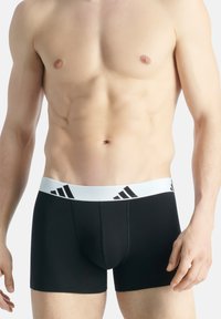 Boxer briefs pretos com uma faixa elástica branca que apresenta accents de logotipo pretos. Tecido suave, design ajustado, comprimento até a coxa.