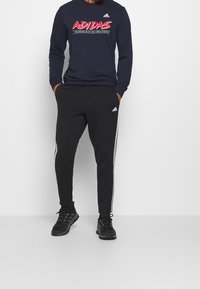 Pantaloni sportivi neri con strisce bianche ai lati e una cintura elastica. Completati da una maglietta a maniche lunghe blu navy con un logo grafico.