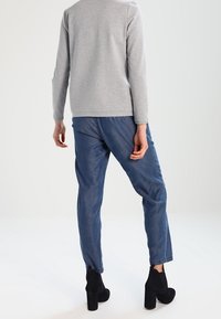 Maglia grigia a maniche lunghe abbinata a jeans blu a sigaretta e stivaletti neri con tacco, che mostrano un outfit semplice e informale.