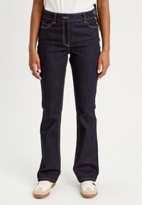 Dark blue denim jeans with a fitted waist, flared legs, and contrast stitching details. Paired with white sneakers.