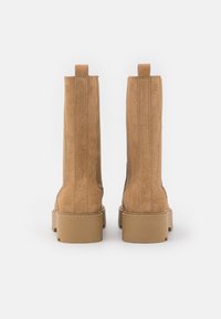 Tan suede ankle boots with a smooth finish, rectangular toe, flat sole, and two pull tabs at the back. Stitch detailing along the seams.