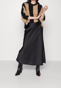 Beige und schwarz gestreifter Strickpullover, kombiniert mit einem eleganten schwarzen Satin-Maxikleid und figurbetonenden schwarzen Kn�öchelstiefeln. Glatte Textur insgesamt.
