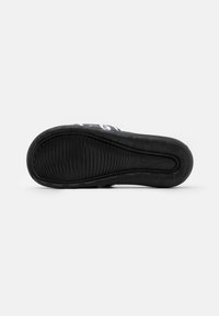 Svart sneakersåle med en teksturert gummidesign, som har en glatt midtseksjon og fremtredende spor for grep. Nike-logoen er til stede.