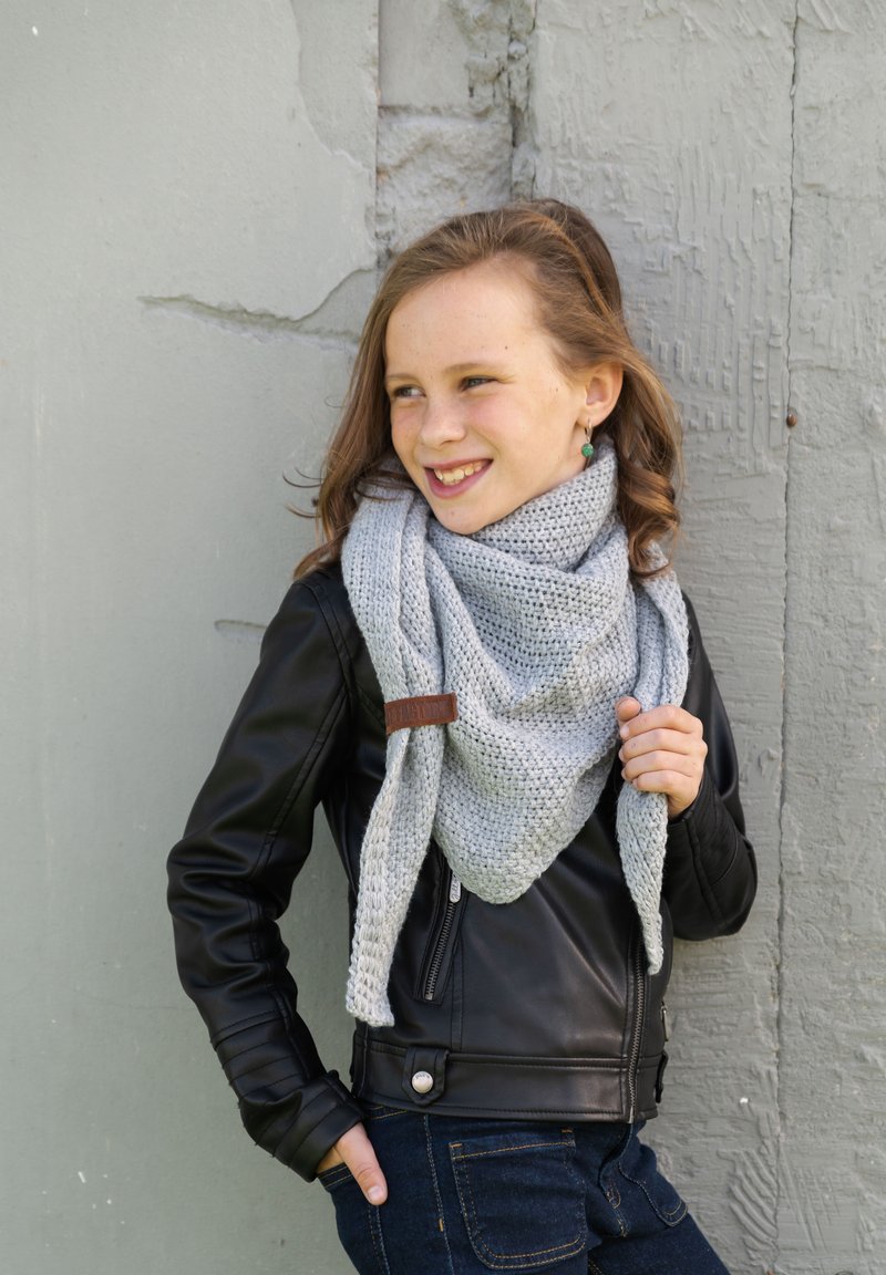 Grijze gebreide sjaal in een driehoekige vorm, om de nek gedrapeerd, met een bruin leren accent. Draagt een zwart leren jack.