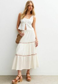 Witte geborduurde crop top, gelaagde maxi rok met bloemaccenten, en bruine platform sandalen. Een geweven handtas maakt de look compleet.