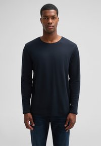 Langärmliges marineblaues T-Shirt aus weicher Baumwolle. Verfügt über einen runden Ausschnitt und eine glatte Textur. Kombiniert mit dunklen Jeans.