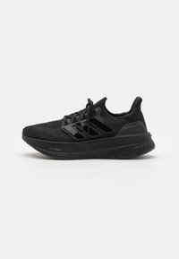 Černá běžecká obuv Adidas Ultraboost s pleteným svrškem, šněrováním a silnou polstrovanou podrážkou na jednobarevném bílém pozadí.