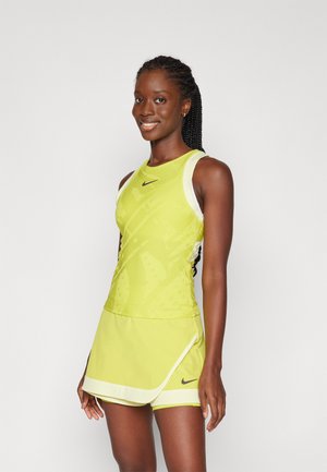 Débardeur de sport jaune vif avec des accents blancs, présentant un motif texturé. Accompagné d'une jupe enroulée assortie. Logo Nike affiché.