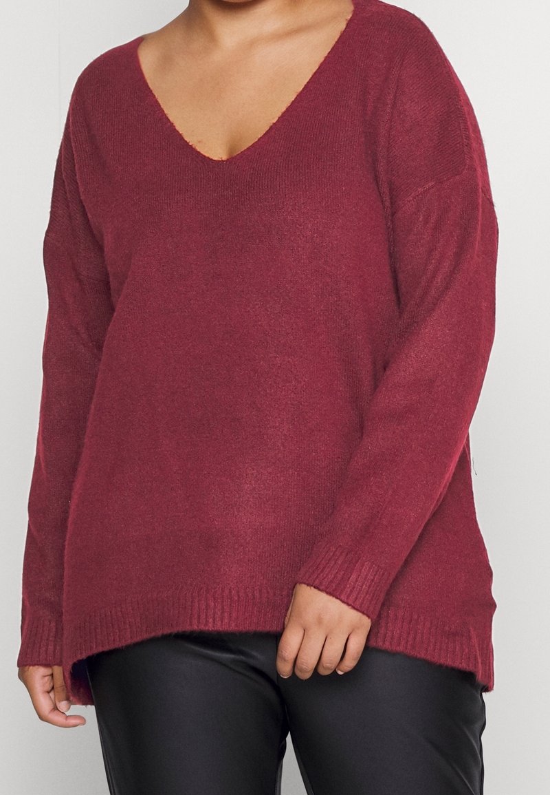 Burgunderfarbener Strickpullover mit V-Ausschnitt, langen Ärmeln und geripptem Saum. Hat einen lockeren Sitz und Seitenschlitze für zusätzliche Bewegungsfreiheit. Weicher Stoff.