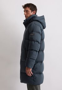 Granatowa puchowa kurtka z kapturem, z poziomym przeszyciem, zamykaną na zamek boczną kieszenią oraz naszywką z logo na rękawie.