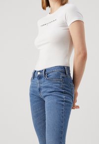 Camiseta blanca de algodón con el logo "TOMMY JEANS" en negro, combinada con unos pantalones vaqueros ajustados de mezclilla azul con un diseño clásico de cinco bolsillos.