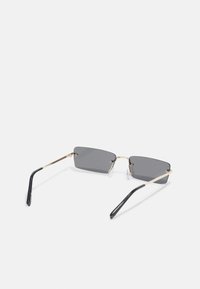 Ochelari de soare rectanguli cu lentile gri, cadru din metal auriu și brațe din plastic negru. Prezintă pad-uri pentru nas transparente și articulații detaliate.