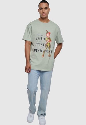 Lys grønn bomull t-skjorte med et grafisk bilde av en karakter og teksten "TRO, TILLIT, FE-STØV." Kombinert med lyseblå jeans og hvite sneakers.