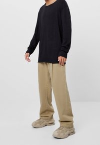 Czarna koszula z długim rękawem, o luźnym kroju, z zaokrąglonym dekoltem. Do tego beżowe spodnie o lu�źnym kroju i beżowe masywne sneakersy.