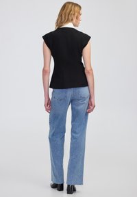 Czarny dopasowany top bez rękawów z białym kołnierzykiem, w komplecie z jasnoniebieskimi spodniami typu high-waisted. Gładka tekstura i elegancki krój.