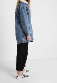 Denimjakke med kunstpelskrave, blå farve, løs pasform, kombineret med sorte bukser og sort-hvide ternede slip-on sko.