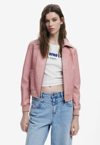 Helles rosa, kurz geschnittenes Jacket mit Reißverschluss, seitlichen Taschen und gerippten Bündchen, kombiniert mit einem weißen Shirt und hellblauen, hoch taillierten Jeans.