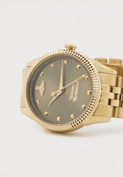 Χρυσό ρολόι χειρός με στεφάνη διακοσμημένη με πυραμίδες, μαύρο καντράν, χρυσούς δείκτες, λογότυπο Vivienne Westwood και μεταλλικό μπρασελέ, που δείχνει ώρα 7:00:10.