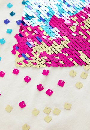 Surface en sequins colorés présentant des nuances de rose, d'or et de bleu, avec un design texturé sur un fond blanc. Petits sequins dispersés visibles.