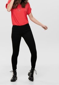 Červené tričko s krátkým rukávem v kombinaci s černými skinny džíny a černými šněrovacími kotníkovými botami. Hladká tkanina, přiléhavý střih, minimalistický styl.