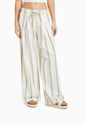 Woman wearing wide-leg white pants with vertical beige stripes and a drawstring waist, paired with white platform sandals.