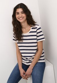 T-shirt rayé en beige clair et marine, avec un col rond et des manches courtes, associé à un jean bleu. Texture lisse, design décontracté.
