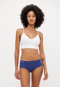 Valge ribaga bralette õhukeste rihmadega, millele on sobitatud tumesinised hipster aluspüksid, millel on õmmeldud serv ja logotagi vöökohta.