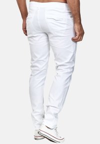 Weiße Baumwollhosen mit schmaler Passform, ausgestattet mit Gesäßtaschen und gesteppten Details. Kombiniert mit weißen Sneakers, die einen lässigen Stil zeigen.