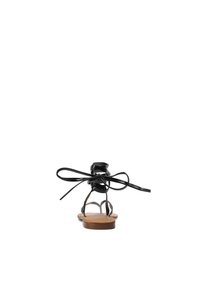 Sandali neri in pelle con punta rotonda, cinturini sottili e dettaglio di lacci legati sul tallone. La suola è piatta e di colore marrone.