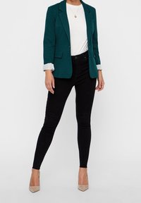 Teal blazer met aangeknipte revers, witte T-shirt, zwarte skinny jeans en beige hoge hakken, met een slim fit en textiel met structuur.