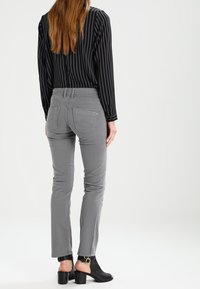 Pantalones gris ajustados con bolsillos traseros cosidos, llevados con una camisa de manga larga a rayas negra y tacones abiertos negros. Textura de tela suave.